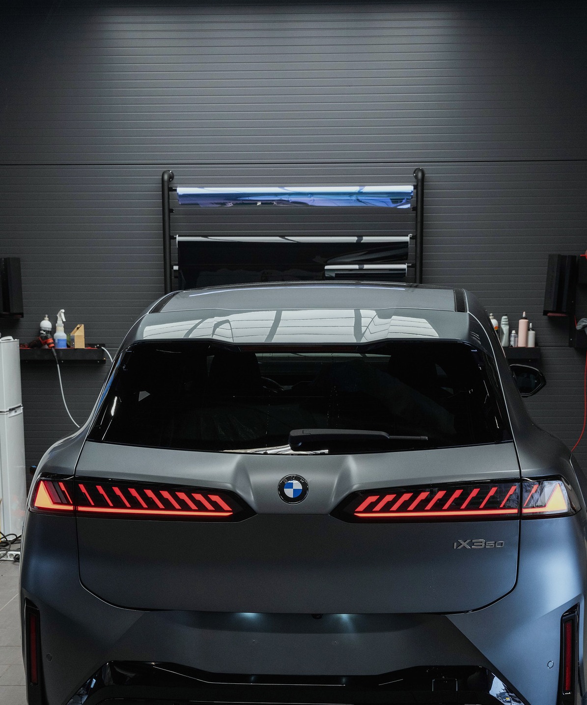 BMW iX3 i matt grå, sett rett bakfra med lyslista tent
