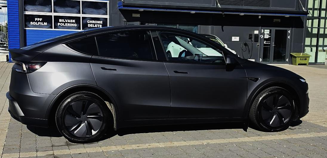 Tesla Model Y i matt grå, i profil utenfor verkstedet